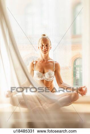 Stock Image - Mid adult woman in yoga position, in front of window. Fotosearch