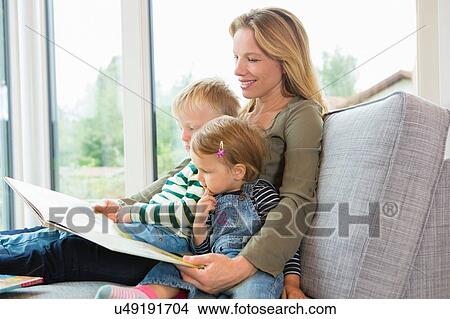 Mother and two young children sitting on sofa reading a book View Large Photo Image Picture - Mother and two young children sitting on sofa reading a book. Fotosearch