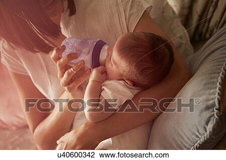 Stock Image - Mother feeding baby in arms. Fotosearch
