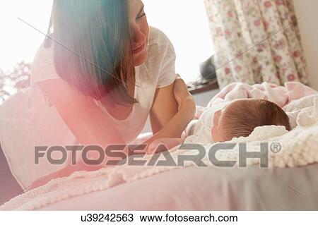 Stock Image - Mother playing with baby in bed. Fotosearch