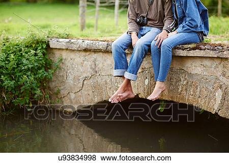Neck down view of young couple sitting on river footbridge View Large Photo Image Stock Photo - Neck down view of young couple sitting on river footbridge. Fotosearch