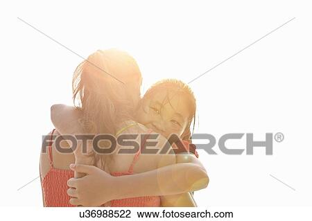 Stock Image - Over the shoulder sunlit view of girl hugging mother. Fotosearch