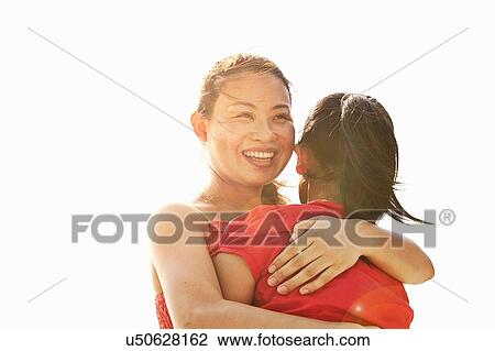 Stock Image - Over the shoulder sunlit view of woman hugging daughter. Fotosearch