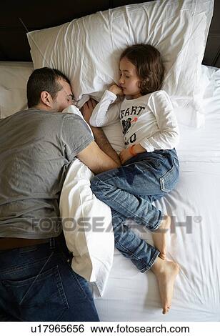 Stock Photograph - Overhead view of father and daughter sleeping on bed. Fotosearch
