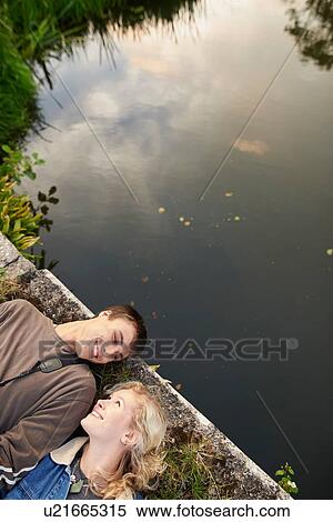 Stock Photography - Overhead view of young couple lying on river footbridge. Fotosearch