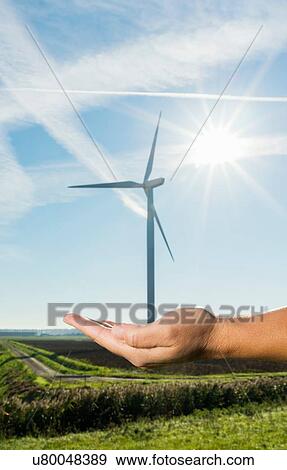 Stock Photo - Person holding out hand as if holding wind turbine in hand, focus on hand. Fotosearch