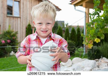 Stock Photography - Portrait of boy in garden carrying stack of bowls. Fotosearch