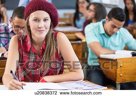 Stock Image - Portrait of female student, sitting at desk in classroom. Fotosearch