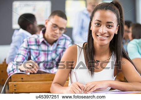 Stock Image - Portrait of female student, sitting at desk in classroom. Fotosearch