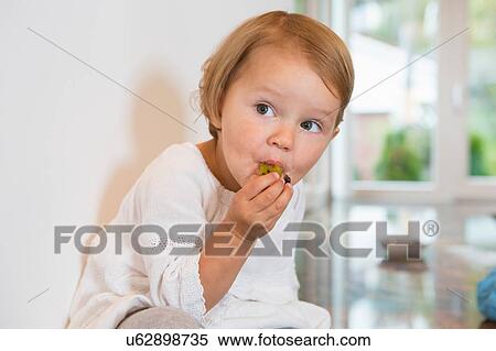 Portrait of female toddler eating plum in kitchen View Large Photo Image Stock Photography - Portrait of female toddler eating plum in kitchen. Fotosearch