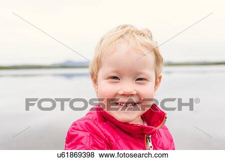 Stock Photo - Portrait of female toddler wearing pink anorak in front of lake, Hafravatn, Iceland. Fotosearch