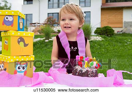 Stock Photography - Portrait of female toddler with birthday cake and pink ribbons in garden. Fotosearch