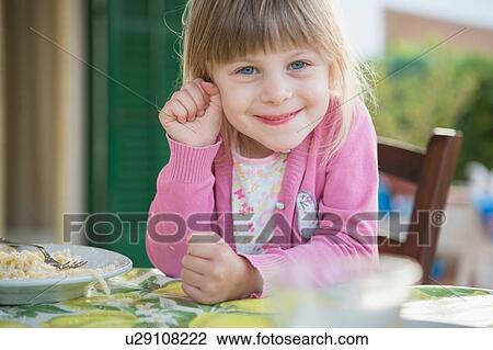 Stock Image - Portrait of girl having breakfast at table. Fotosearch