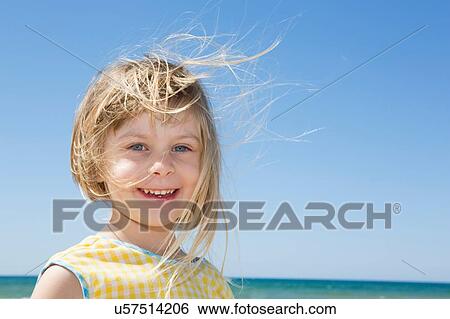 Stock Photograph - Portrait of girl with blond flyaway hair on beach. Fotosearch