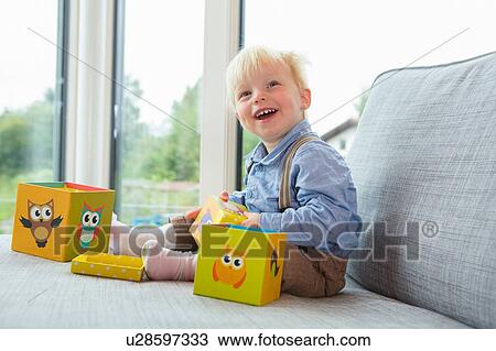 Stock Image - Portrait of happy male toddler playing with building blocks on sofa. Fotosearch