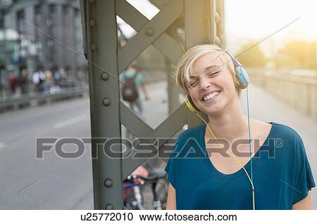 Portrait of happy young woman wearing headphones on bridge View Large Photo Image Stock Image - Portrait of happy young woman wearing headphones on bridge. Fotosearch
