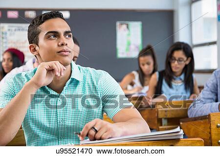 Stock Image - Portrait of male student, sitting at desk in classroom. Fotosearch