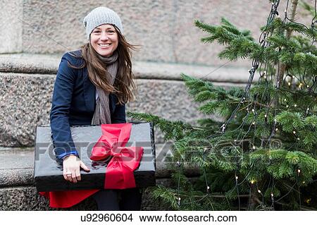 Portrait of mature woman with Christmas gift next to Christmas tree View Large Photo Image Picture - Portrait of mature woman with Christmas gift next to Christmas tree. Fotosearch