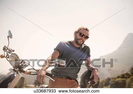 Stock Image - Portrait of mid adult man standing beside moped. Fotosearch