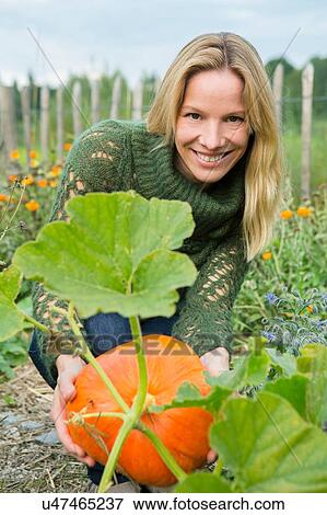 Stock Photo - Portrait of mid adult woman tending pumpkin in garden. Fotosearch