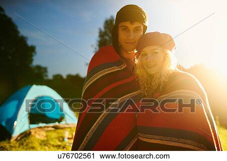 Stock Image - Portrait of romantic young camping couple wrapped in blanket at sunset. Fotosearch