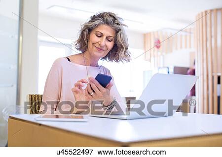 Stock Photo - Portrait of senior female designer texting on smartphone in office. Fotosearch