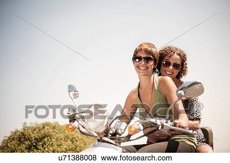 Stock Photo - Portrait of two women sitting on moped. Fotosearch