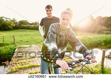 Portrait of young couple on bicycle at river footbridge View Large Photo Image Stock Image - Portrait of young couple on bicycle at river footbridge. Fotosearch