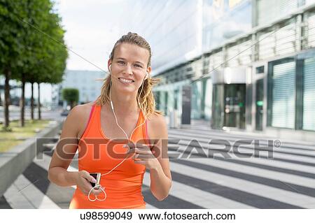 Portrait of young female runner wearing earphones in city View Large Photo Image Stock Photo - Portrait of young female runner wearing earphones in city. Fotosearch