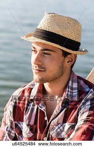 Picture - Portrait of young man wearing straw hat looking away. Fotosearch