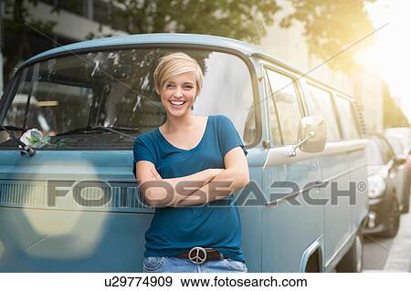 Stock Photo - Portrait of young woman leaning against parked campervan. Fotosearch