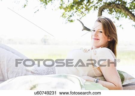 Stock Image - Portrait of young woman reclining on daybed at safari lodge, Kafue National Park, Zambia. Fotosearch