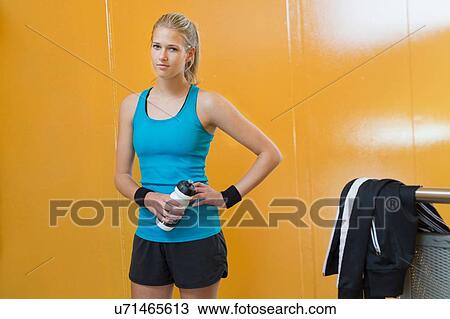 Stock Image - Portrait of young woman, wearing sports clothing, holding water bottle. Fotosearch