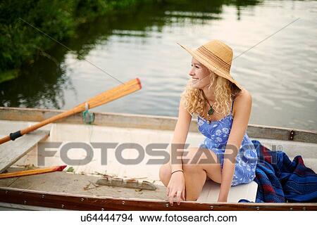 Picture - Portrait of young woman with long blond hair in rowing boat on river. Fotosearch
