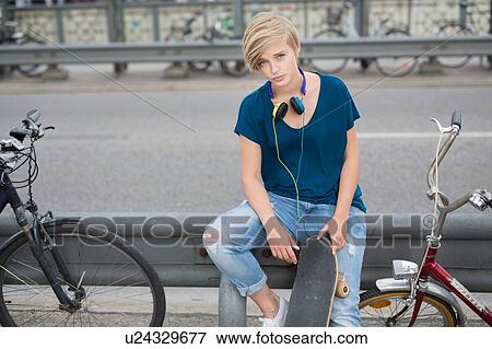 Portrait of young woman with skateboard sitting on barrier View Large Photo Image Stock Photo - Portrait of young woman with skateboard sitting on barrier. Fotosearch