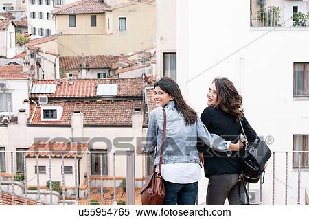 Rear view of lesbian couple standing of roof terrace looking over shoulder at camera smiling, Florence, Tuscany, Italy View Large Photo Image Stock Photography - Rear view of lesbian couple standing of roof terrace looking over shoulder at camera smiling, Florence, Tuscany, Italy. Fotosearch