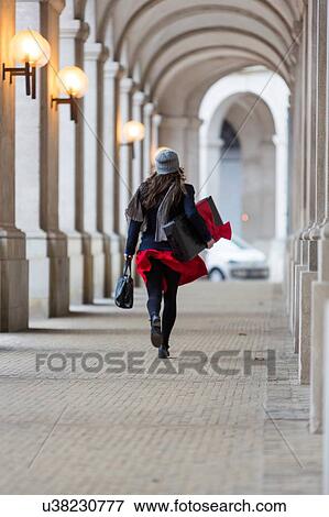 Rear view of mature woman with Christmas gift walking through city colonnade View Large Photo Image Stock Photo - Rear view of mature woman with Christmas gift walking through city colonnade. Fotosearch