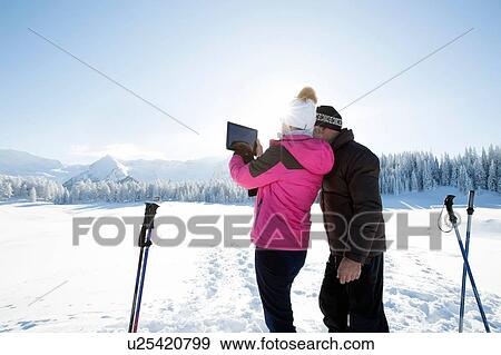 Rear view of senior couple on snowy landscape using digital tablet to take photograph of mountain range, Sattelbergalm, Tyrol, Austria View Large Photo Image Stock Photo - Rear view of senior couple on snowy landscape using digital tablet to take photograph of mountain range, Sattelbergalm, Tyrol, Austria. Fotosearch