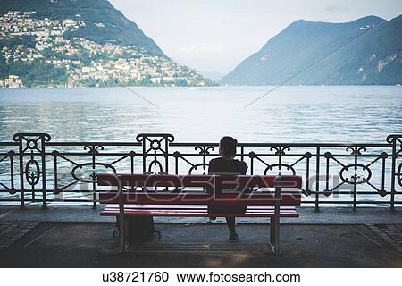 Rear view of silhouetted woman on park bench looking out at Lake Lugano, Switzerland View Large Photo Image Stock Image - Rear view of silhouetted woman on park bench looking out at Lake Lugano, Switzerland. Fotosearch