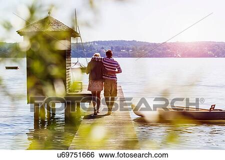 Rear view of young couple walking along pier on lake to boathouse, Schondorf, Ammersee, Bavaria, Germany View Large Photo Image Stock Photograph - Rear view of young couple walking along pier on lake to boathouse, Schondorf, Ammersee, Bavaria, Germany. Fotosearch