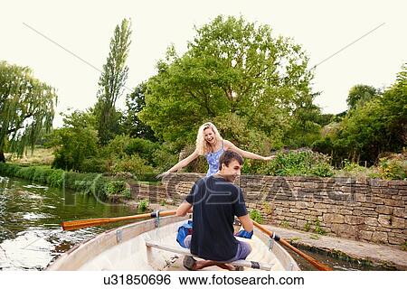Rear view of young woman with boyfriend standing in rowing boat on river View Large Photo Image Stock Photograph - Rear view of young woman with boyfriend standing in rowing boat on river. Fotosearch