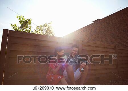 Stock Image - Relaxed mid adult couple chatting and drinking at rooftop party. Fotosearch