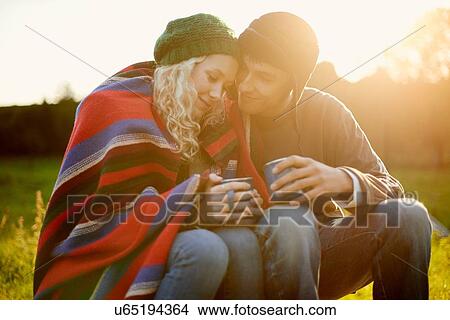 Picture - Romantic young camping couple wrapped in blanket with tea drinks. Fotosearch