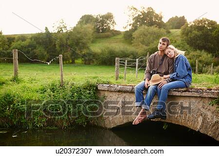 Romantic young couple sitting on river footbridge View Large Photo Image Stock Photo - Romantic young couple sitting on river footbridge. Fotosearch