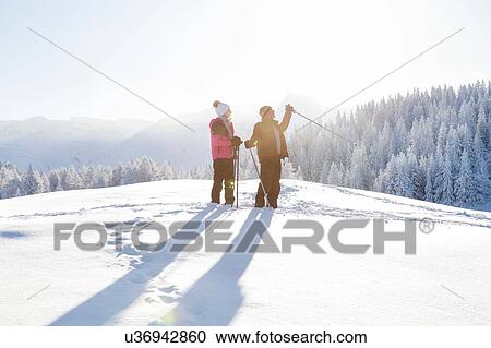 Stock Image - Senior couple on snow covered landscape holding walking poles looking away, Sattelbergalm, Tyrol, Austria. Fotosearch