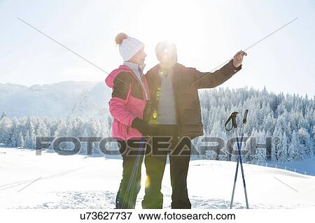Stock Photo - Senior couple on snowy landscape using smartphone to take photograph, Sattelbergalm, Tyrol, Austria. Fotosearch