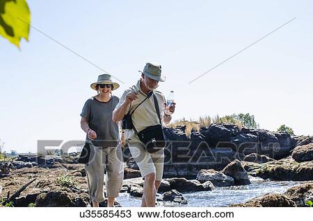 Stock Image - Senior man and wife exploring river rocks, near Victoria Falls, Zambia. Fotosearch