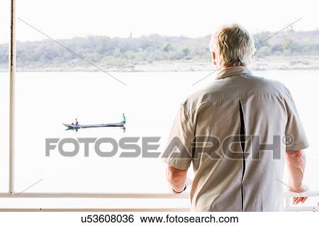 Stock Photograph - Senior man on safari looking out at river, Kafue National Park, Zambia. Fotosearch