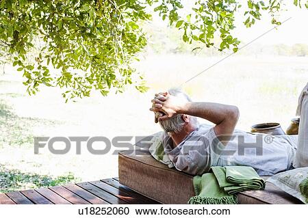 Stock Image - Senior man relaxing on daybed at safari lodge, Kafue National Park, Zambia. Fotosearch