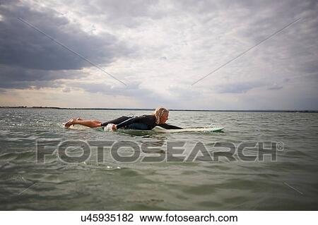 Stock Image - Senior woman on surfboard in sea, paddleboarding. Fotosearch